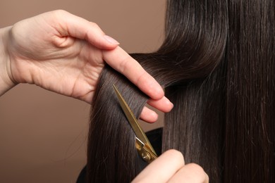 Hairdresser cutting client's hair with scissors on light brown background, closeup