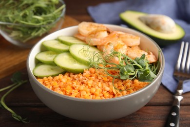 Delicious lentil bowl with shrimps and cucumber on wooden table