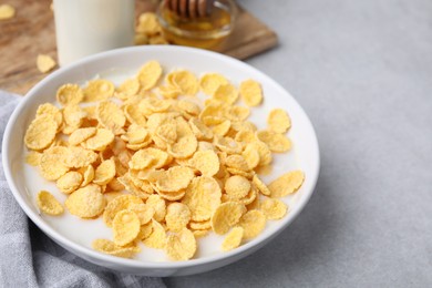 Photo of Breakfast cereal. Corn flakes and milk in bowl on light grey table, closeup. Space for text