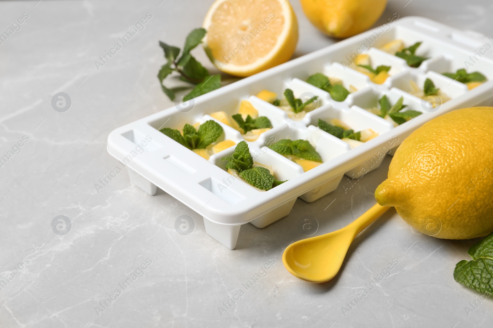 Photo of Spoon, ice cube tray with mint and lemon on grey table