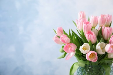 Photo of Beautiful bouquet of tulips in glass vase against light background. Space for text