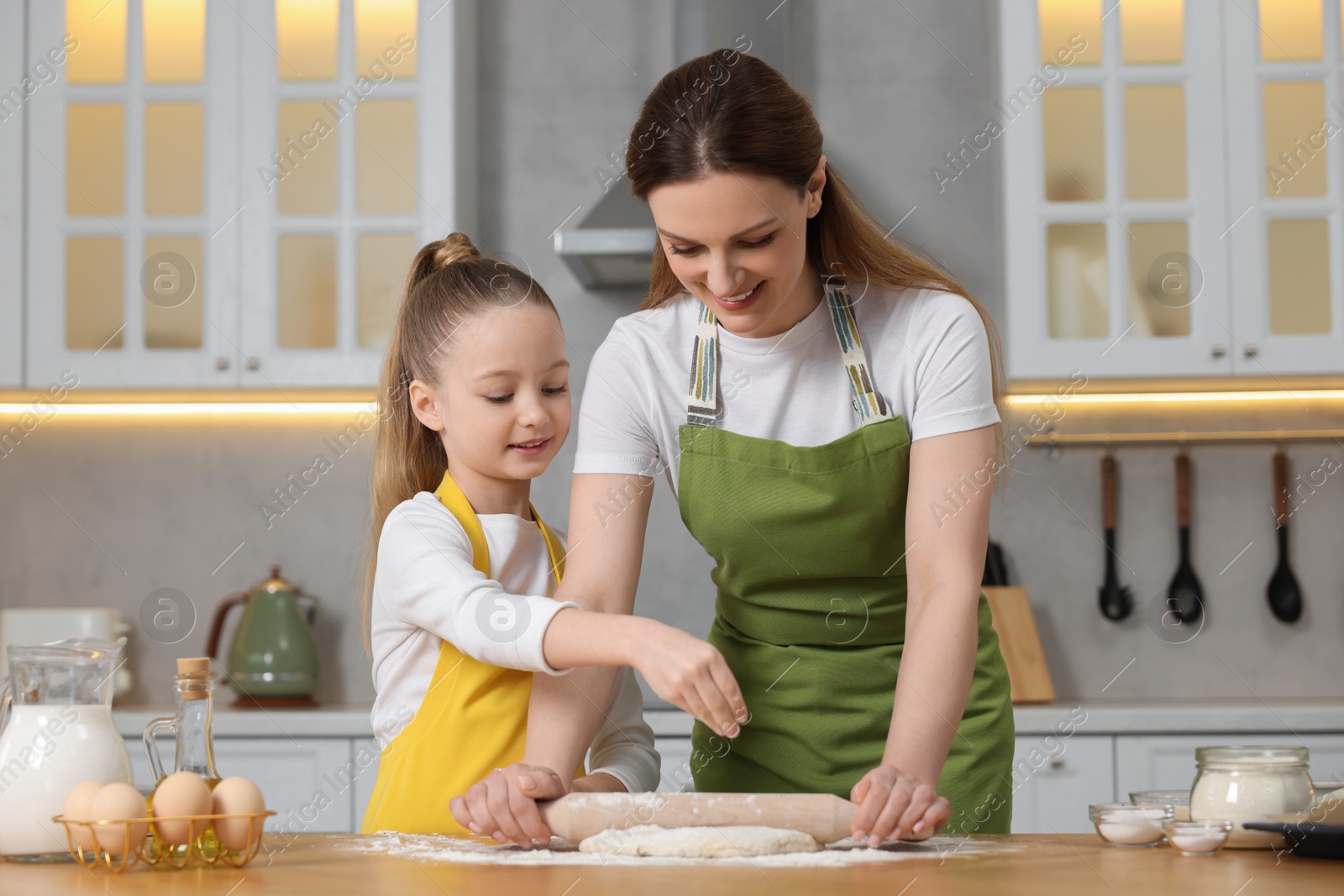 Photo of Making bread. Mother and her daughter rolling dough at wooden table in kitchen