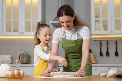 Making bread. Mother and her daughter rolling dough at wooden table in kitchen