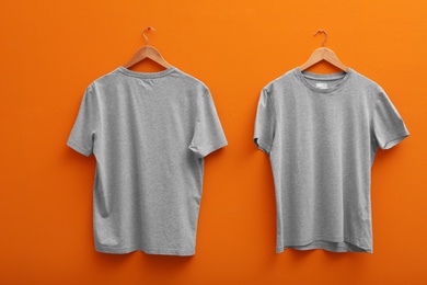 Photo of Hangers with blank t-shirts on color background. Mockup for design