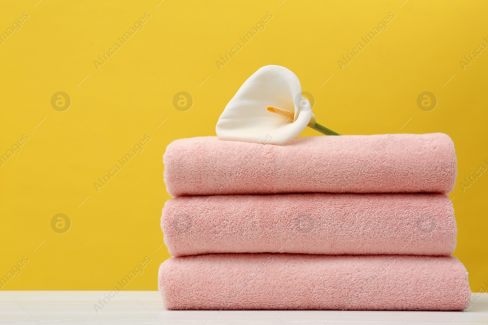 Photo of Stack of soft clean towels with beautiful flower on table against color background. Space for text