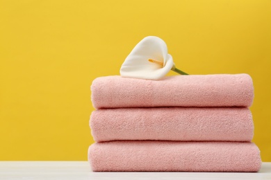 Photo of Stack of soft clean towels with beautiful flower on table against color background. Space for text
