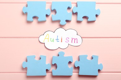 Flat lay composition with jigsaw puzzle pieces and word Autism on pink wooden background