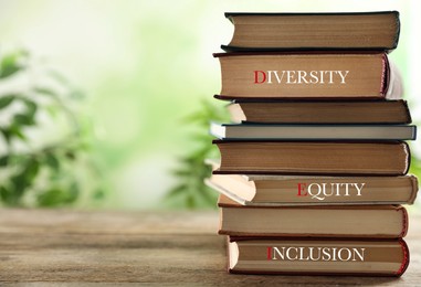 Stack of hardcover books with words Diversity, Equity, Inclusion on wooden table outdoors. Space for text