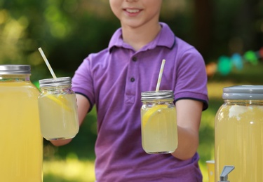 Photo of little boy with natural lemonade in park, closeup. Summer refreshing drink