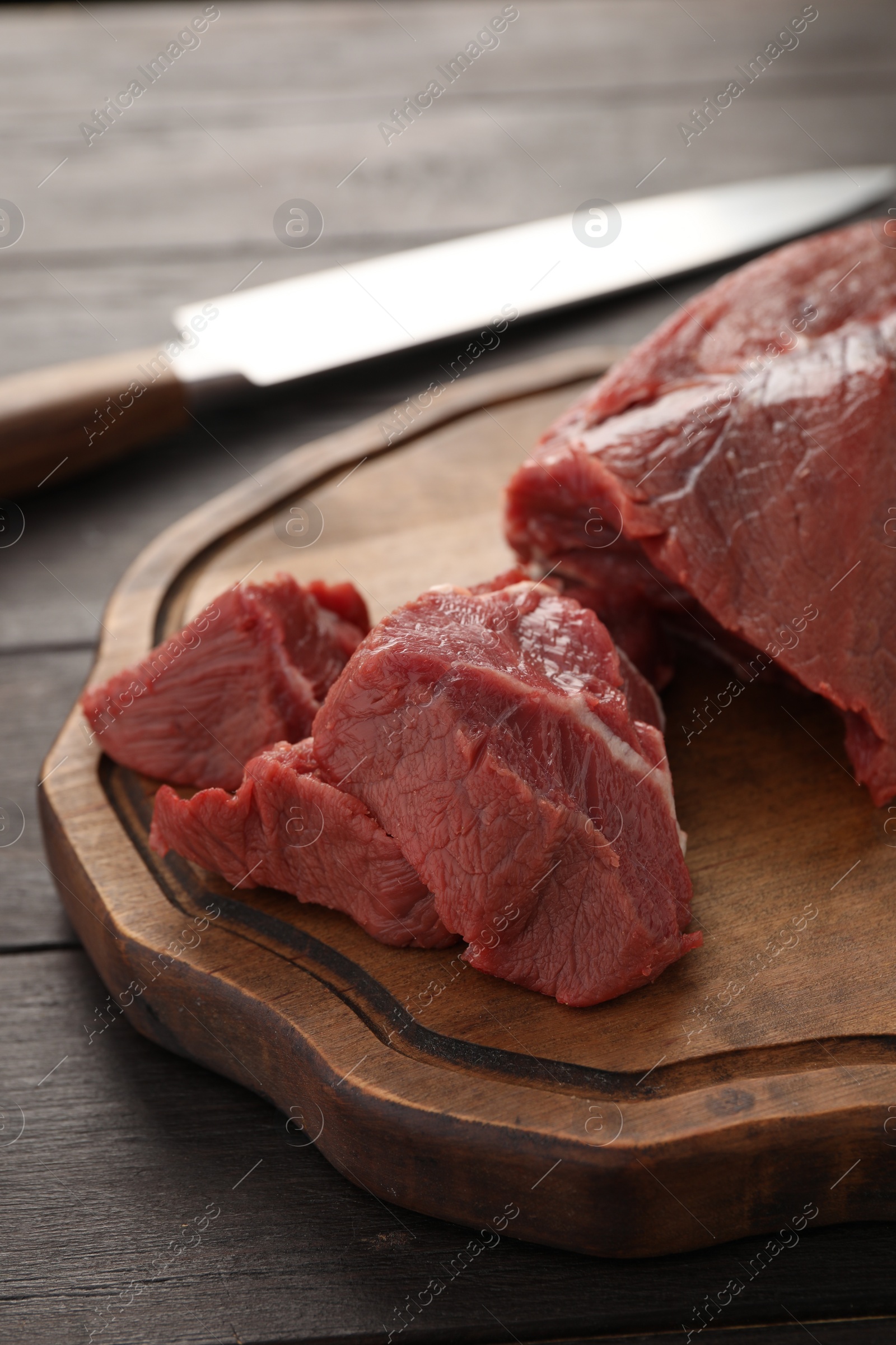 Photo of Pieces of raw beef meat and knife on wooden table, closeup