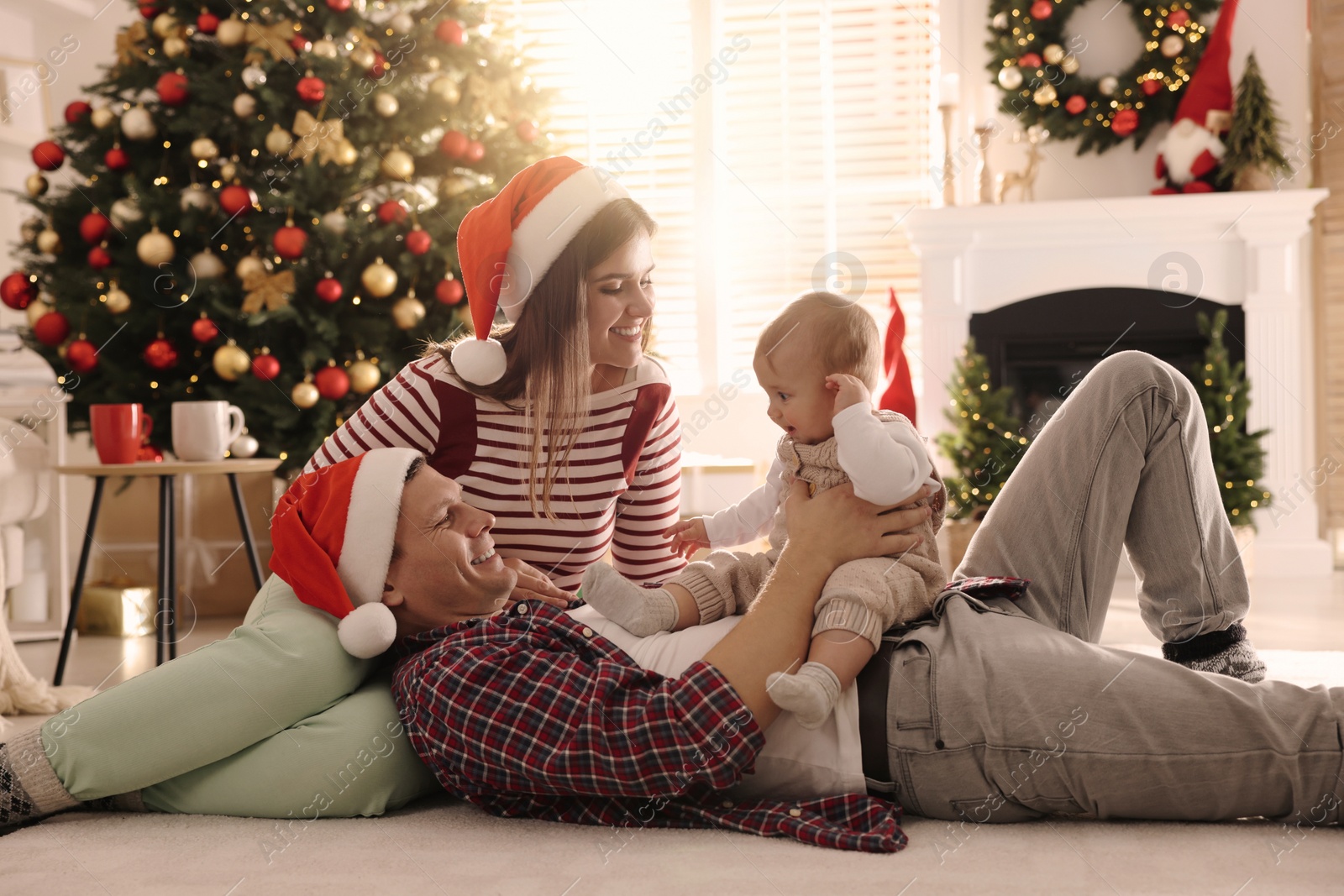 Photo of Happy family with cute baby on floor in room decorated for Christmas