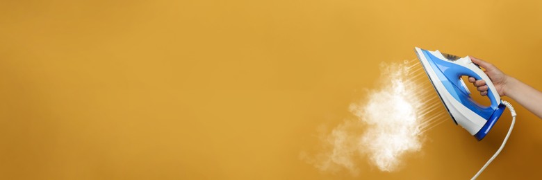 Image of Woman with iron on orange background, closeup. Banner design with space for text