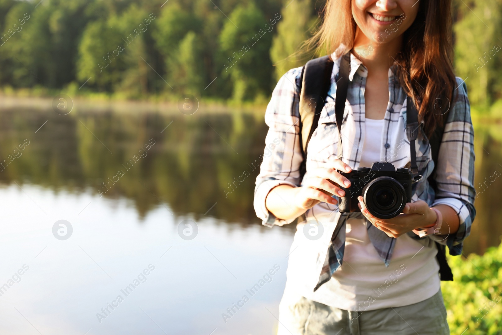 Photo of Young female photographer with camera on shore of lake. Camping season