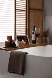 Towel and wooden tray with spa products on bathtub in bathroom, selective focus