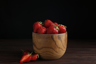 Photo of Delicious ripe strawberries in bowl on wooden table against black background