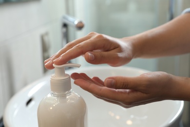 Photo of Woman applying liquid soap on hand in bathroom, closeup