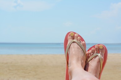 Photo of Woman wearing stylish pink flip flops on beach near sea, closeup. Space for text