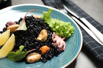 Delicious black risotto with seafood and lemon on plate, closeup