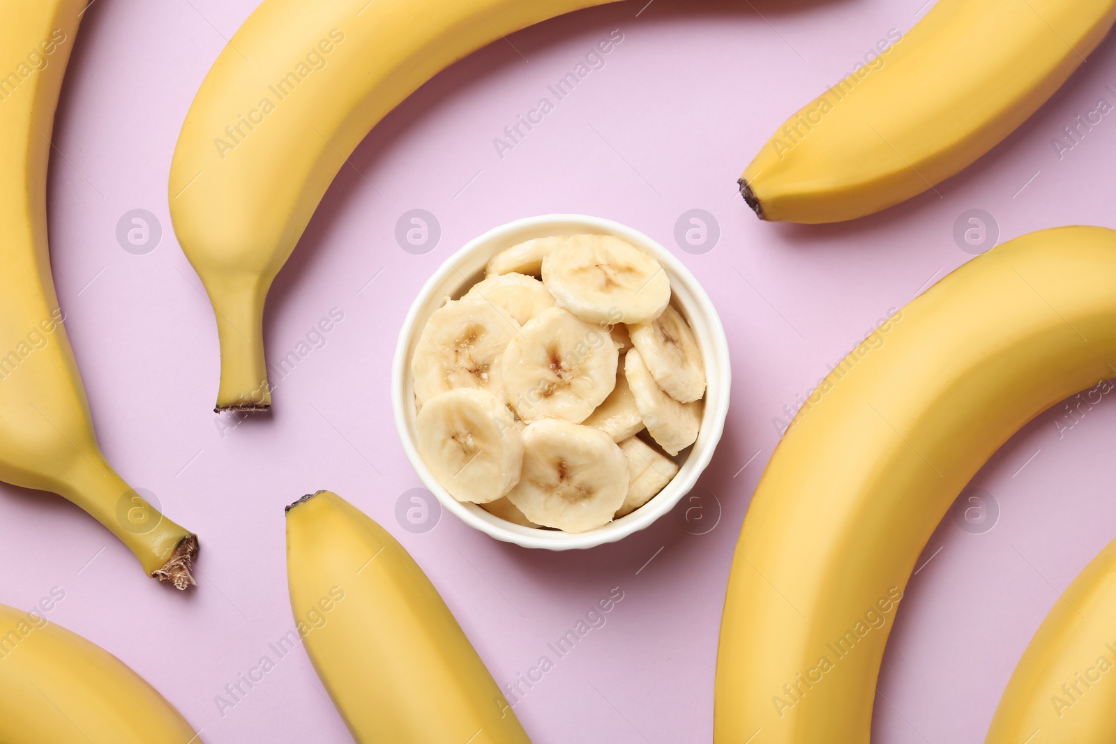 Photo of Bowl with cut bananas and whole fruits on pink background, flat lay