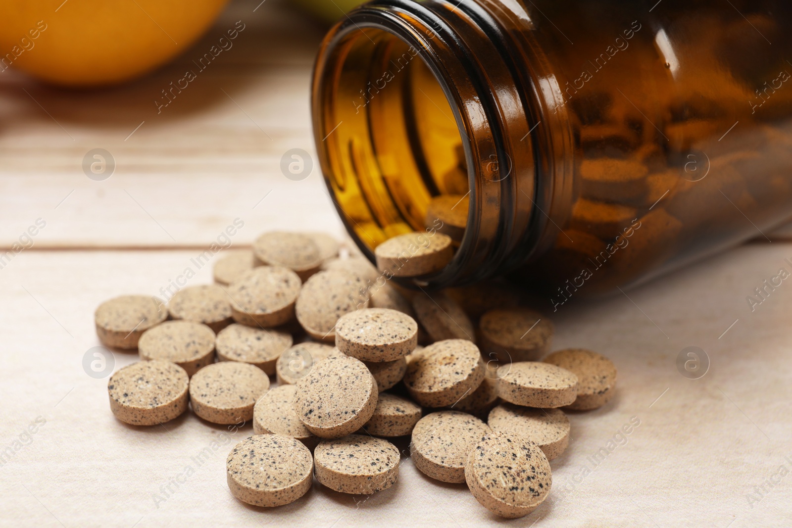 Photo of Dietary supplements. Overturned bottle and pills on light wooden table