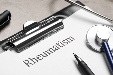 Clipboard with word Rheumatism and stethoscope on light gray table, closeup