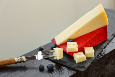 Photo of Different delicious cheeses, fork and blueberries on slate plate, closeup