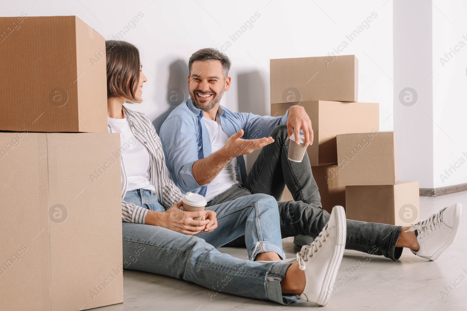 Photo of Happy couple with takeaway coffee resting on floor in new apartment. Moving day