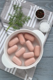 Bowl of delicious sausages, dill, salt and pepper on grey wooden table, flat lay