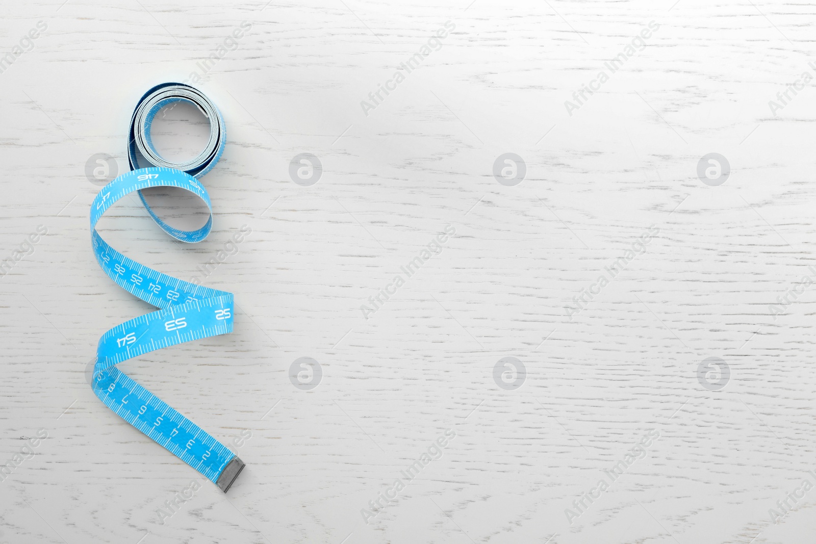 Photo of light blue measuring tape on white wooden table, top view. Space for text