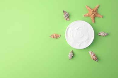 Jar of cream and seashells on light green background, flat lay. Space for text