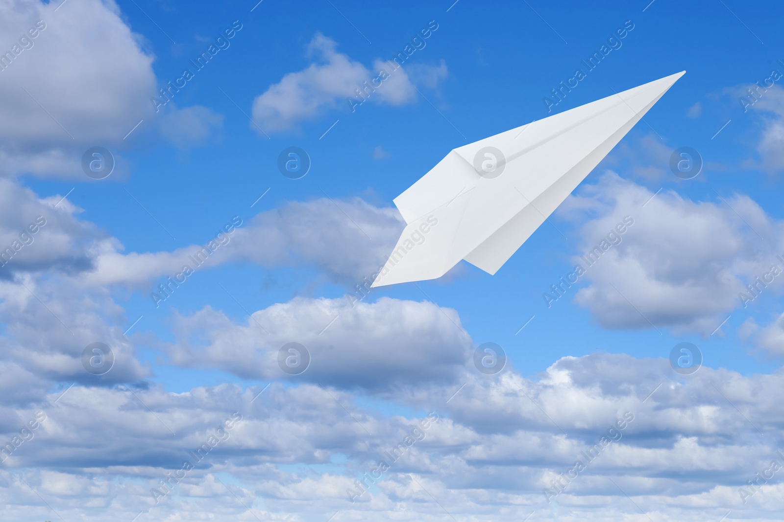 Image of White paper plane flying in blue sky with clouds with clouds