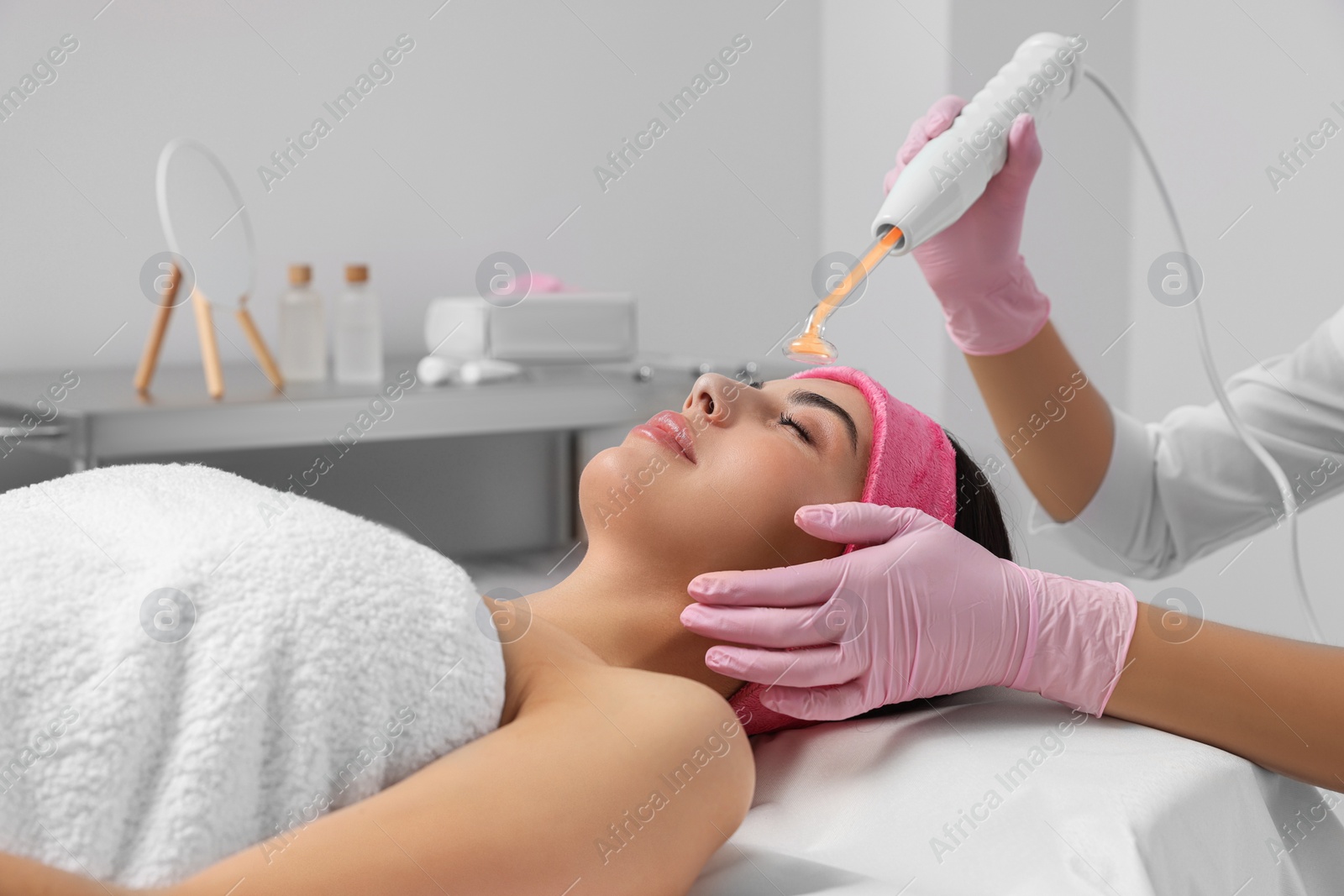 Photo of Young woman undergoing face rejuvenation procedure with darsonval in salon