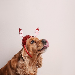 Photo of Adorable Cocker Spaniel dog in Santa headband on light background, space for text