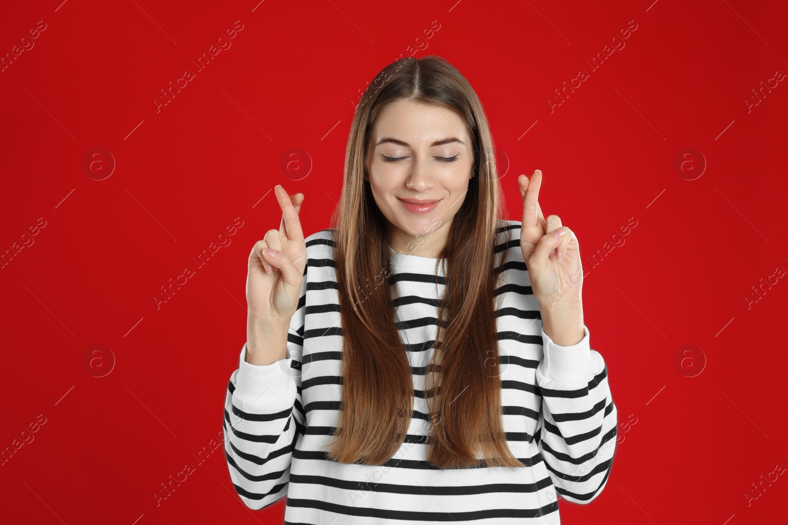 Photo of Woman with crossed fingers on red background. Superstition concept