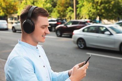 Photo of Smiling man in headphones using smartphone on city street. Space for text