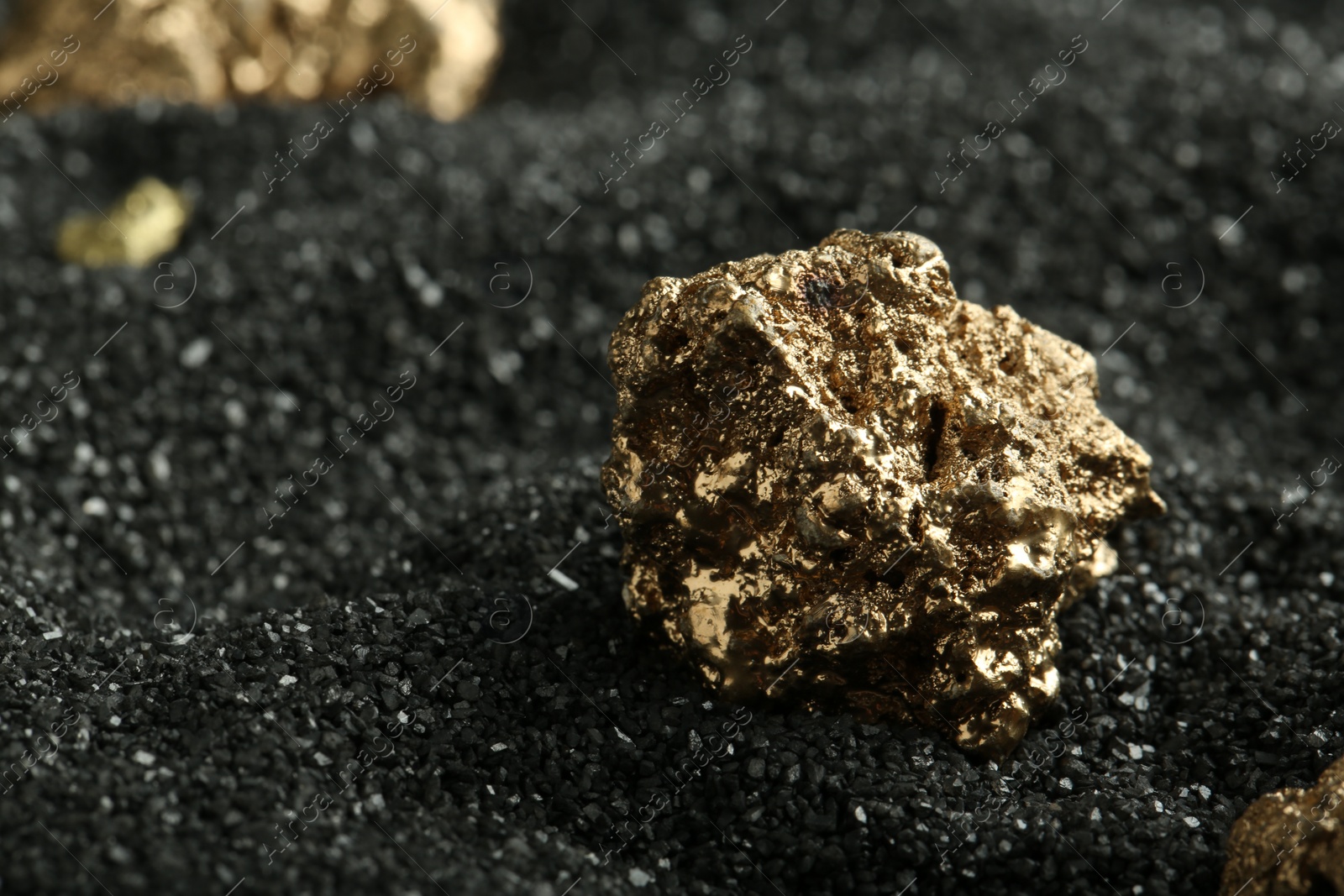 Photo of Shiny gold nugget on black sand, closeup. Space for text