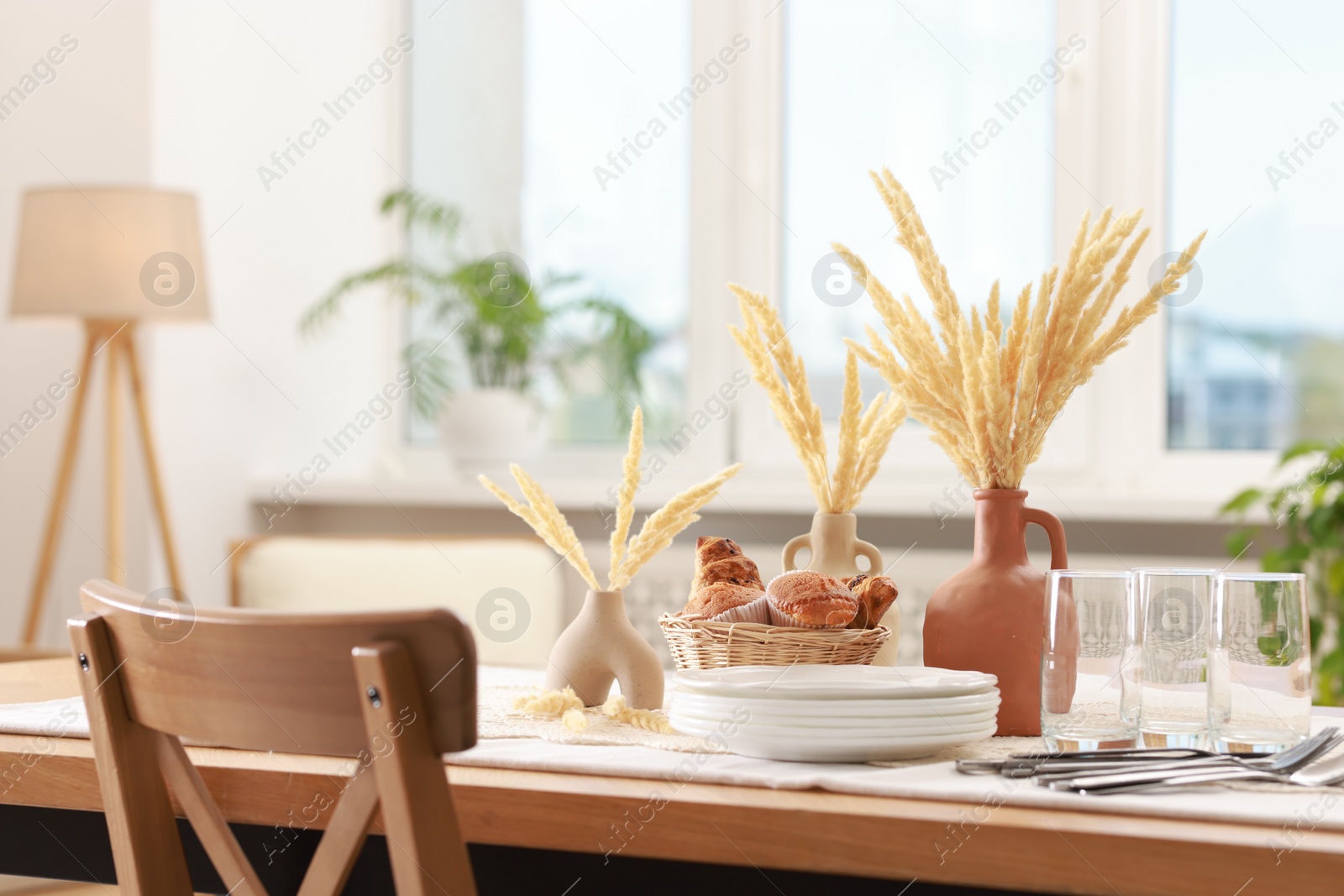 Photo of Clean dishes, dry spikes and fresh pastries on table in stylish dining room