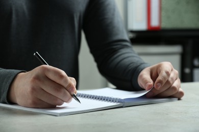 Man writing with pen in notebook at white table indoors, closeup