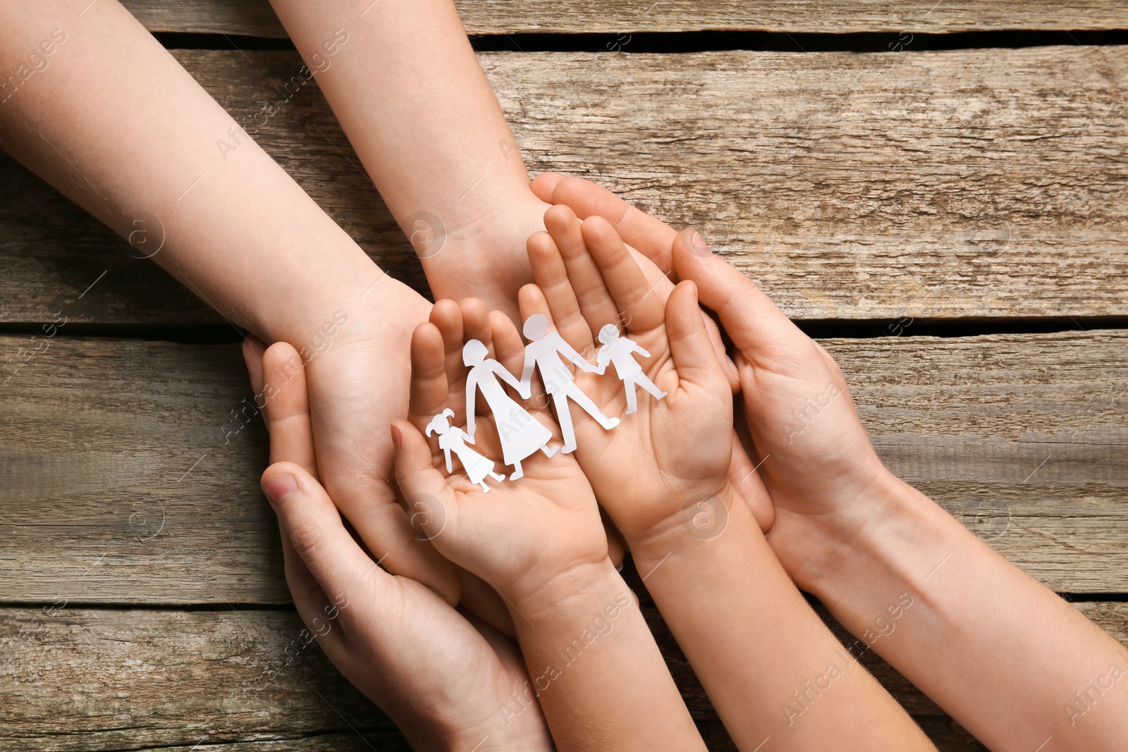 Photo of Parents and child holding paper cutout of family at wooden table, top view