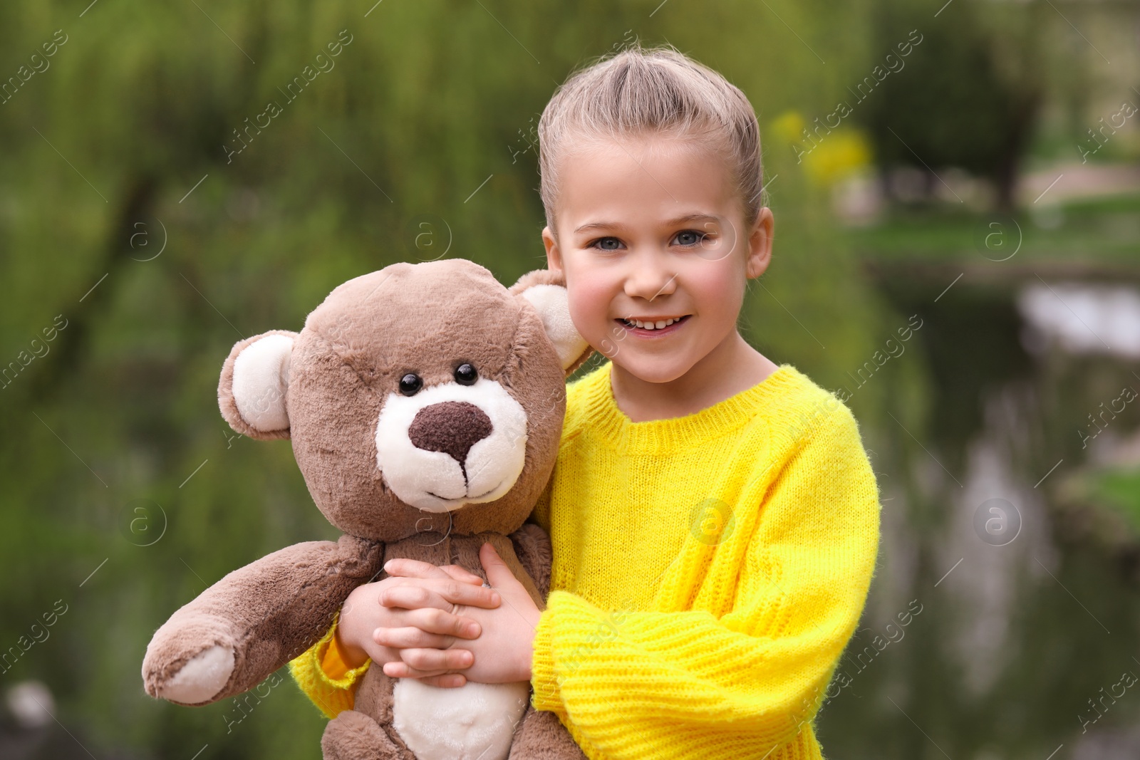 Photo of Cute little girl with teddy bear outdoors