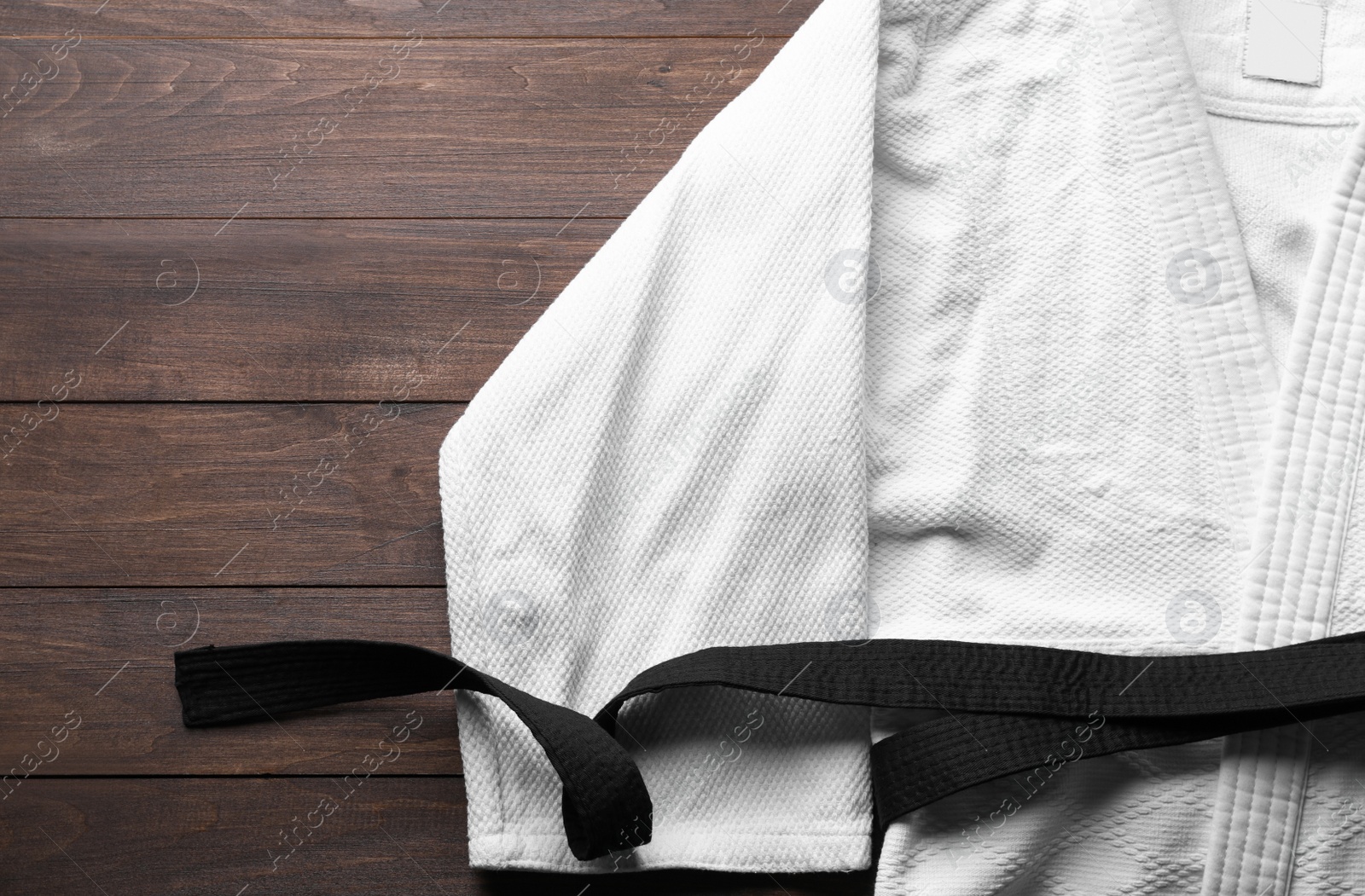 Photo of Martial arts uniform with black belt on white wooden background, top view. Space for text