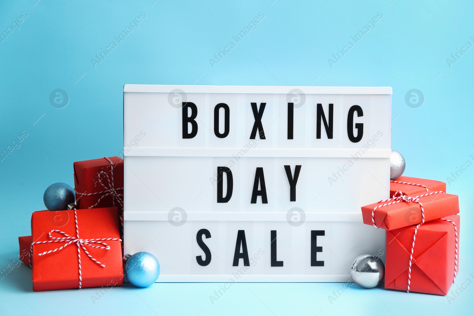 Photo of Lightbox with phrase BOXING DAY SALE and Christmas decorations on light blue background