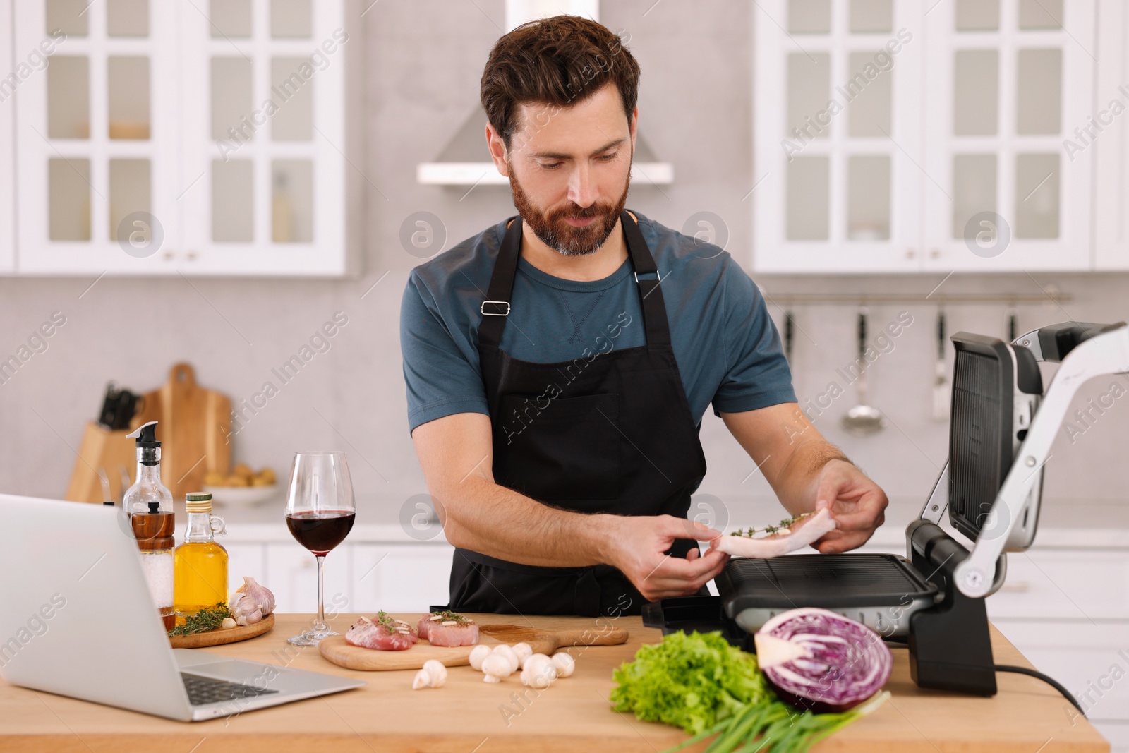 Photo of Man making dinner while watching online cooking course via laptop in kitchen