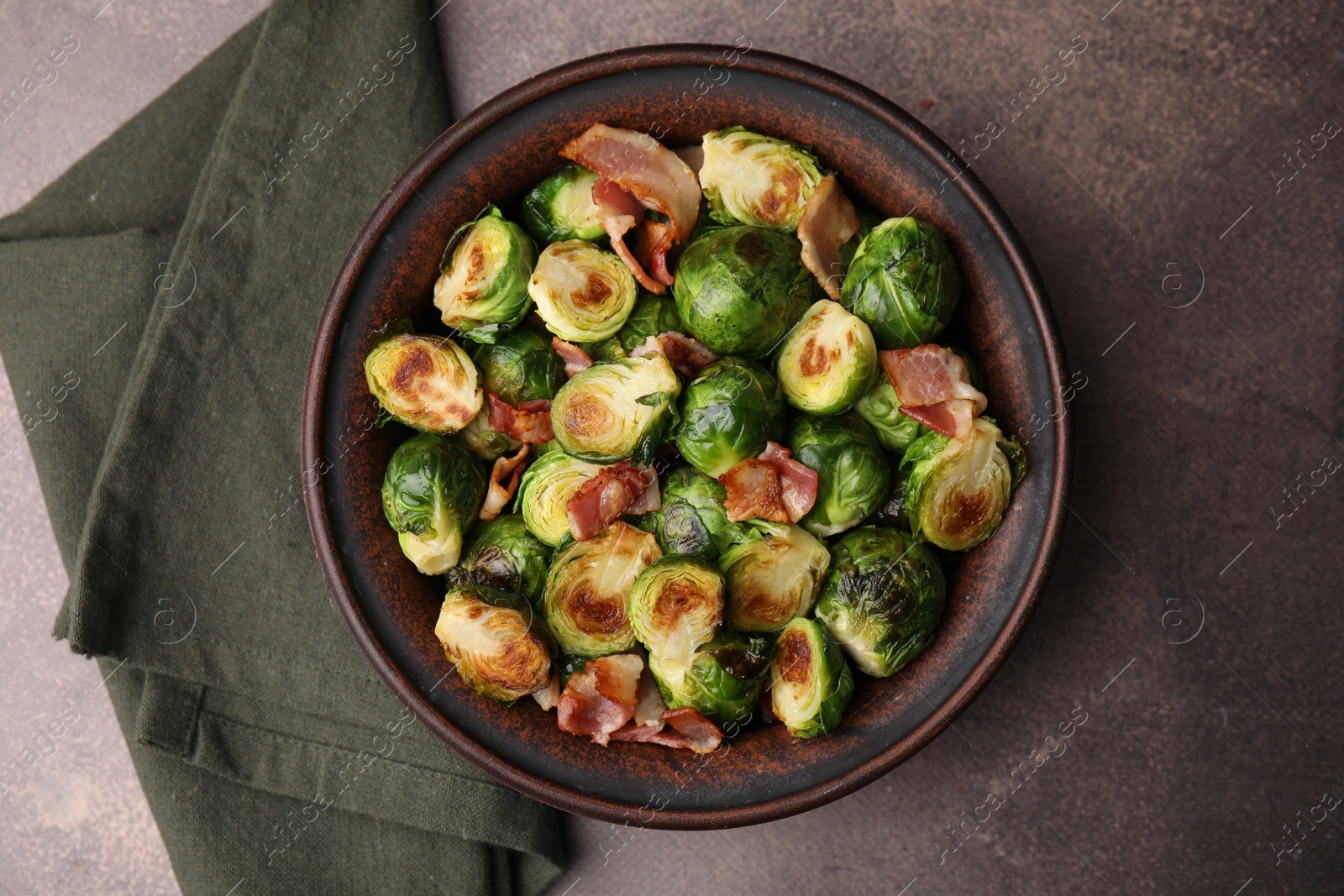 Photo of Delicious roasted Brussels sprouts and bacon in bowl on brown table, top view