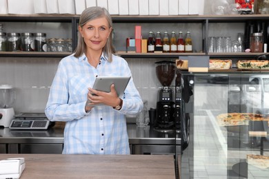 Smiling business owner with tablet at cashier desk in her cafe