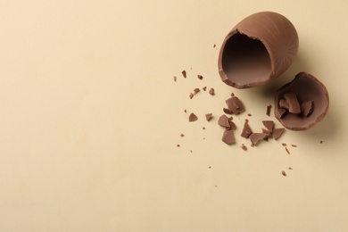 Photo of Broken chocolate egg on beige background, flat lay. Space for text