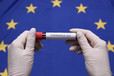 Photo of Doctor holding sample tube with label Coronavirus Test above European Union flag, closeup