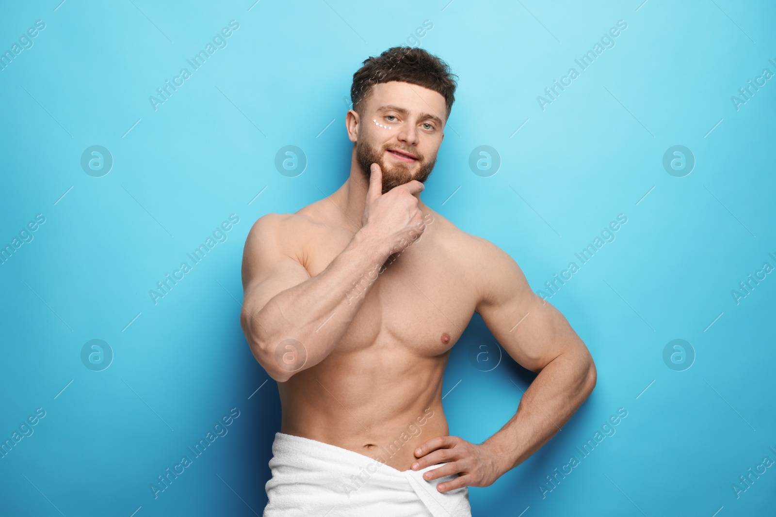 Photo of Handsome man with moisturizing cream on his face against light blue background