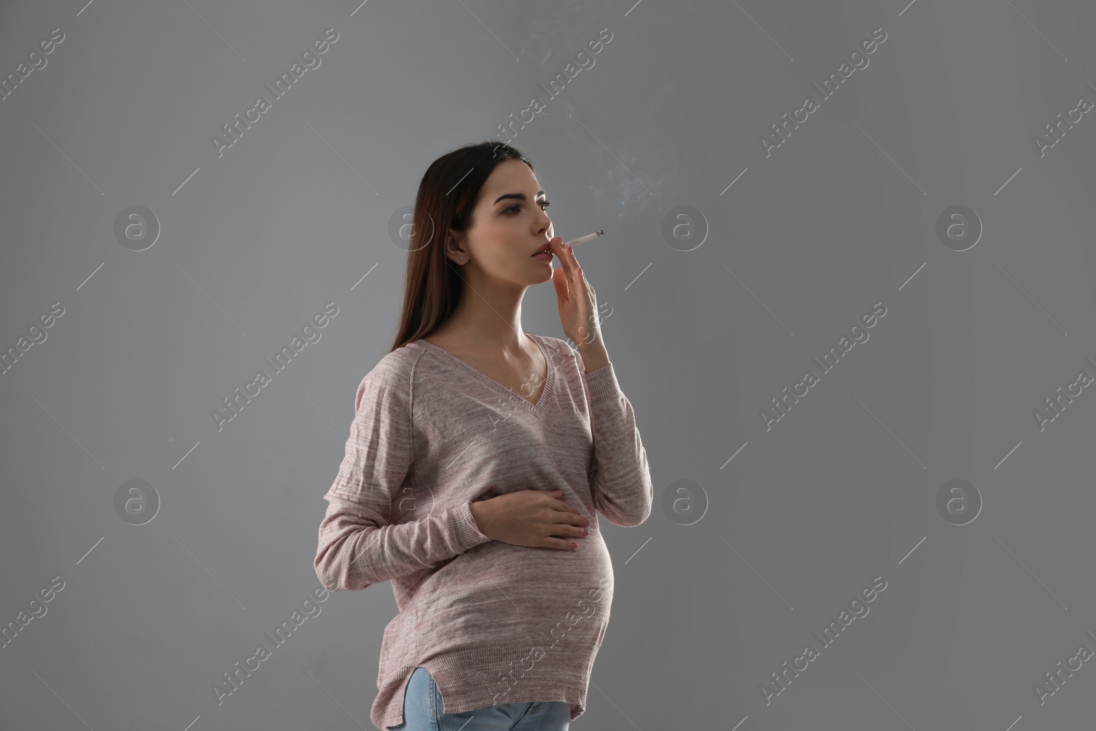 Photo of Young pregnant woman smoking cigarette on grey background