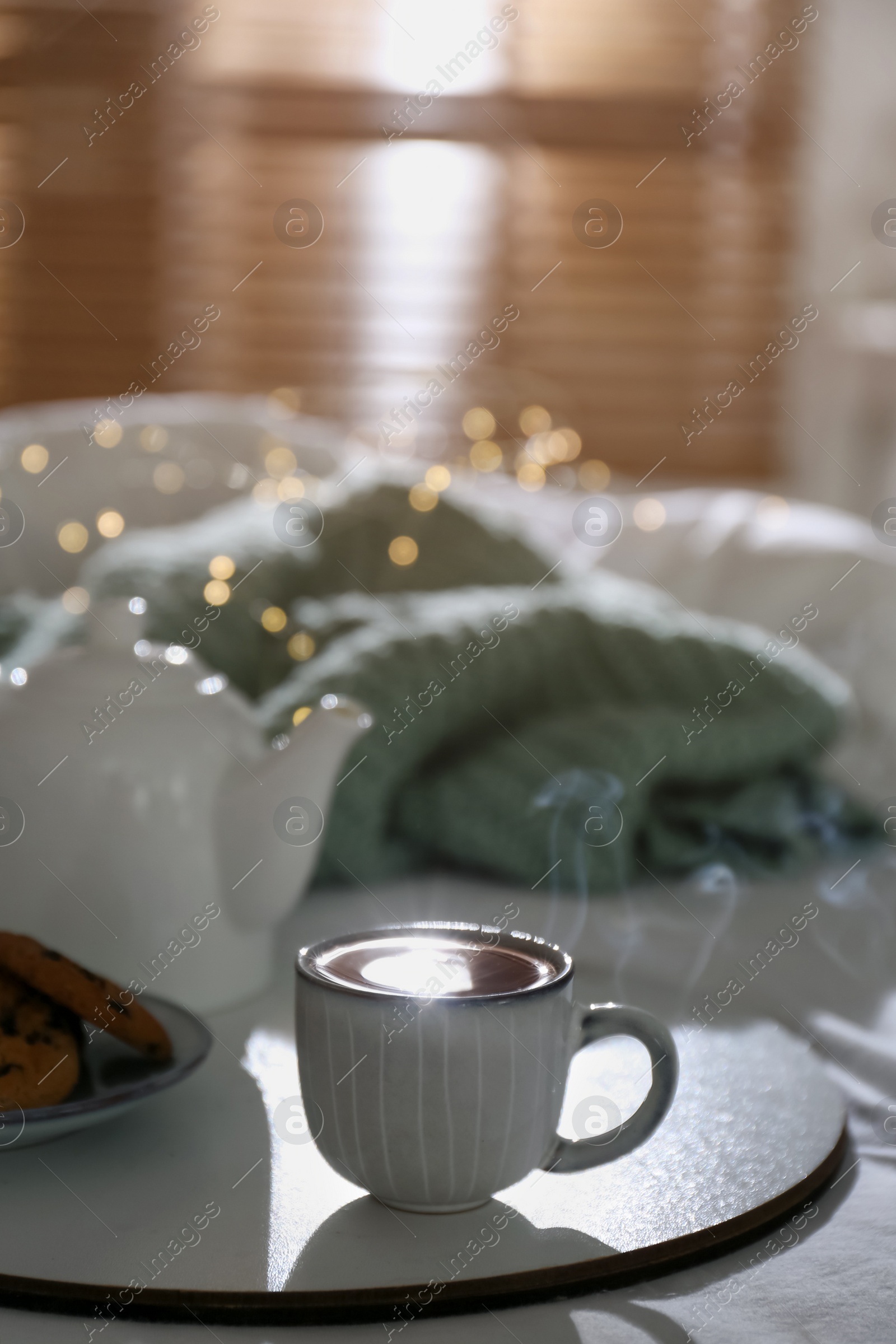 Photo of Tray with cup of hot tea and teapot on bed indoors